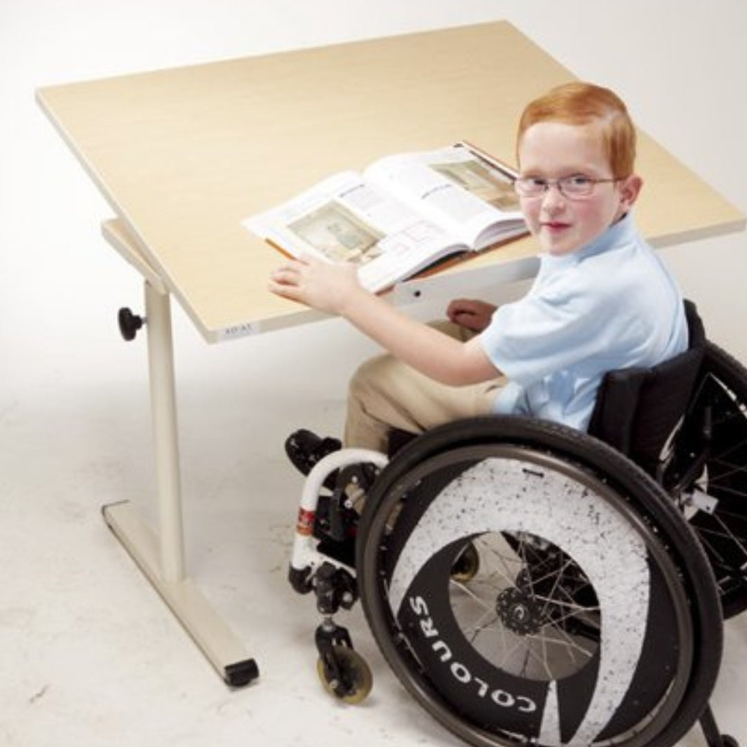a young person in a wheelchair sits at an accessible desk as a book lies open in front of them
