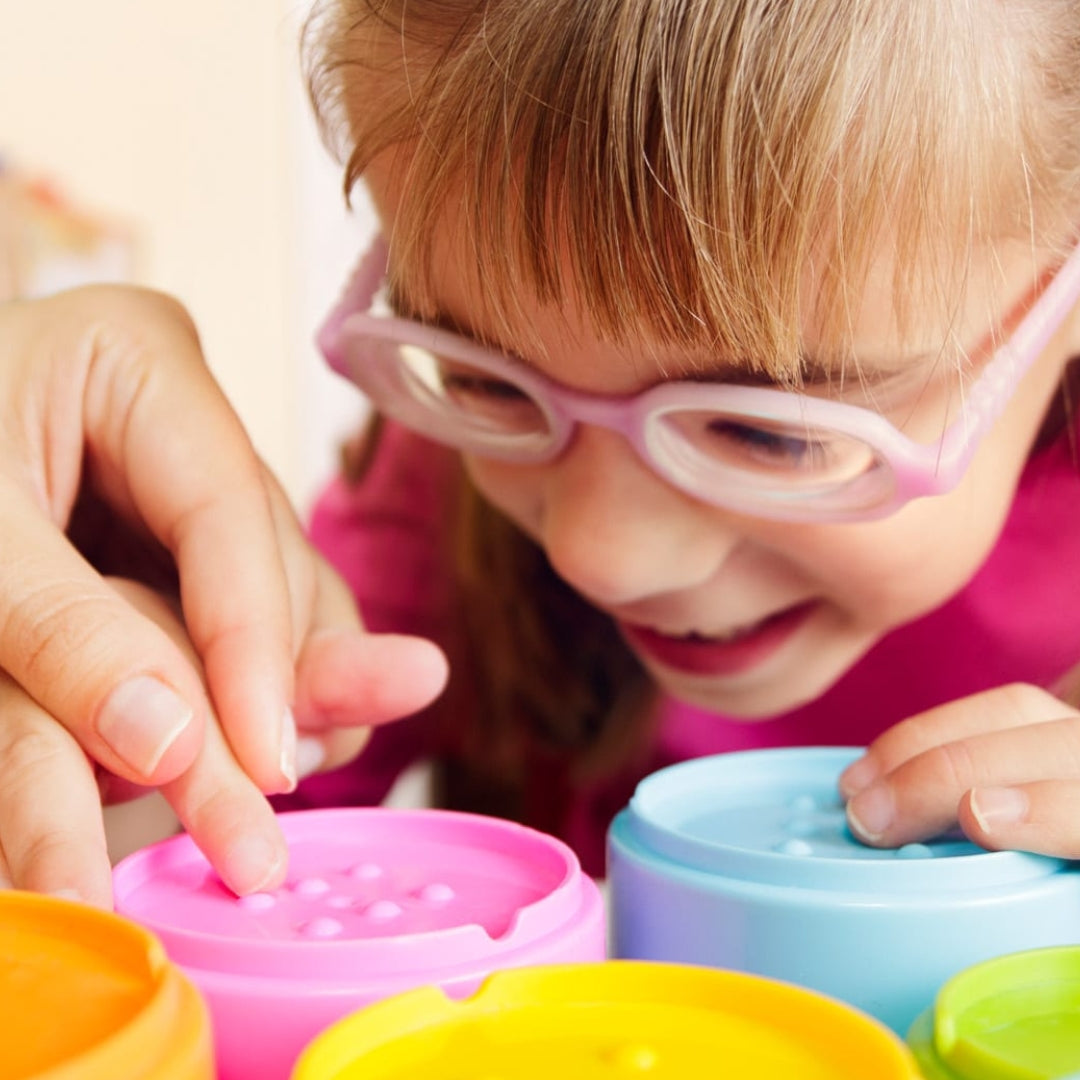 Ayoung girl wearing thick glasses examines a tactile toy that teaches braille