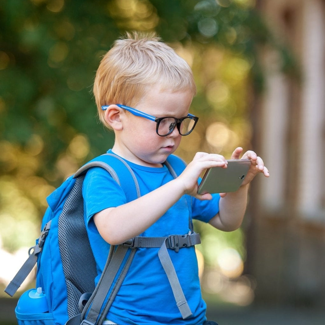 A young boy wearing glasses and a backpack uses a smartphone for magnification