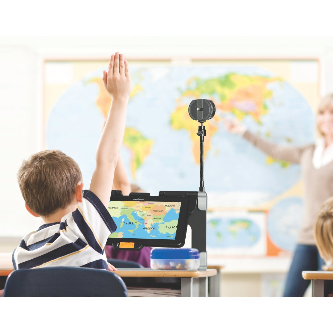 A student in a classroom raises his hand. On his desk is a distance viewer mangnifer to help him read the map at the front of the class.