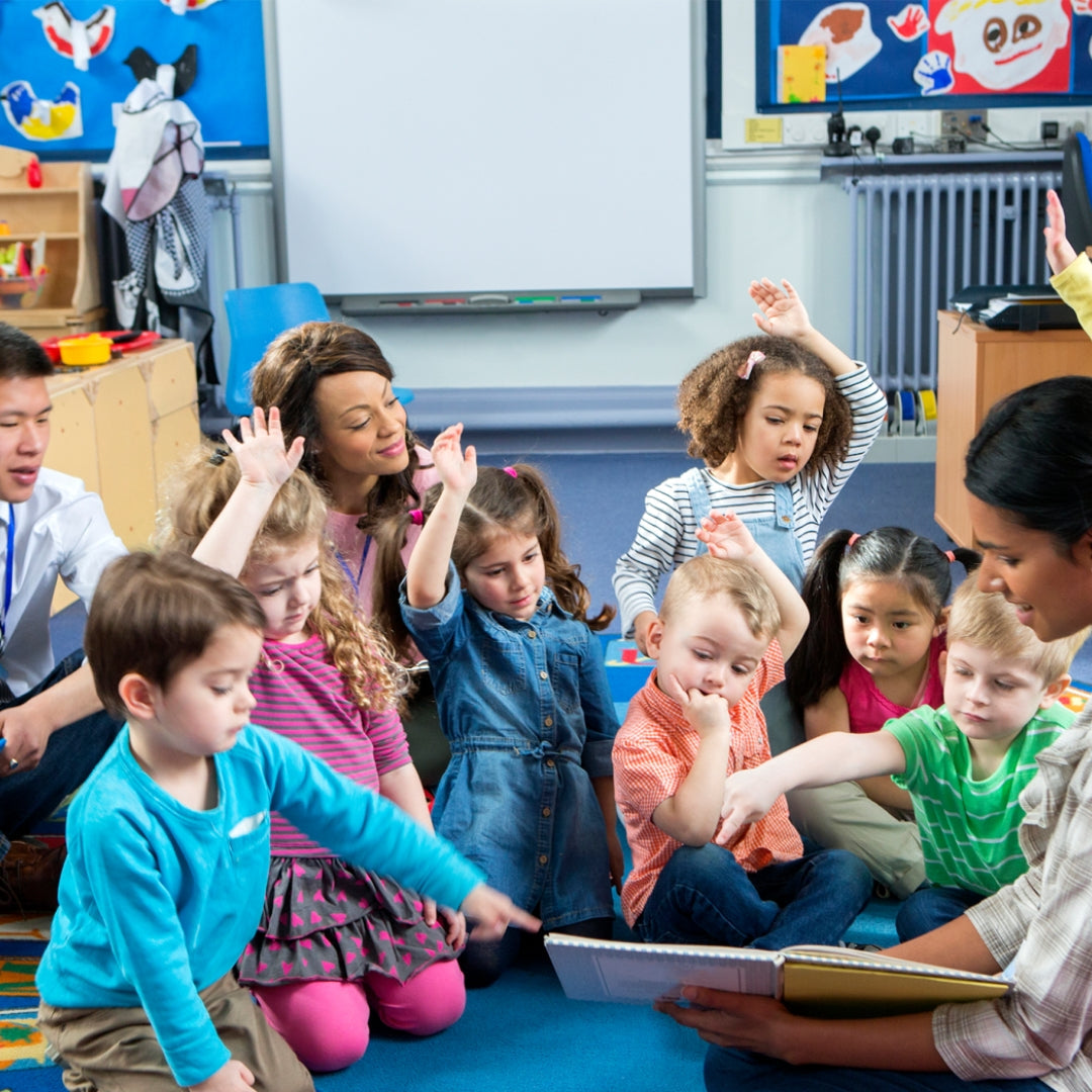 Young children sit on the floor in a circle as a teacher reads to them