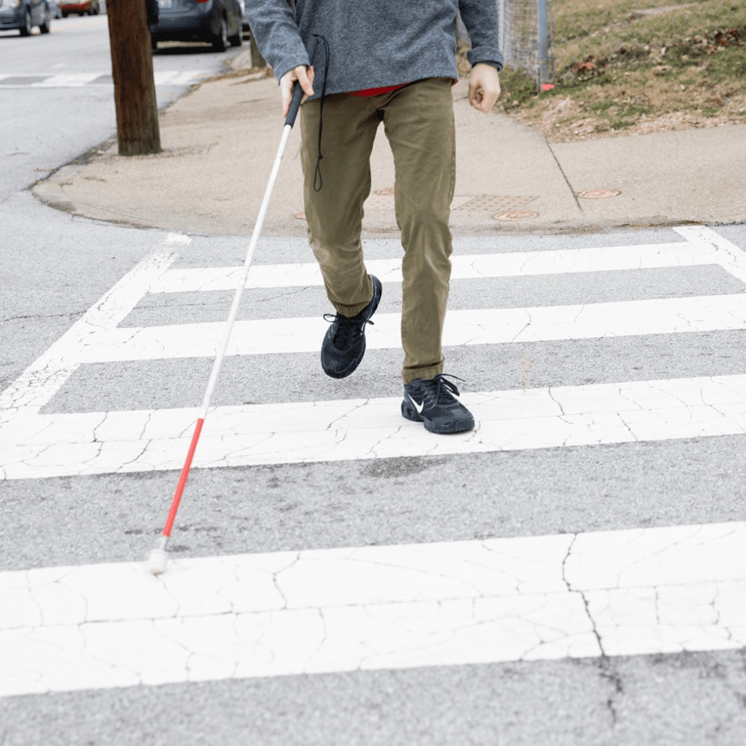 A man uses a mobility cane to cross the street at a crosswalk