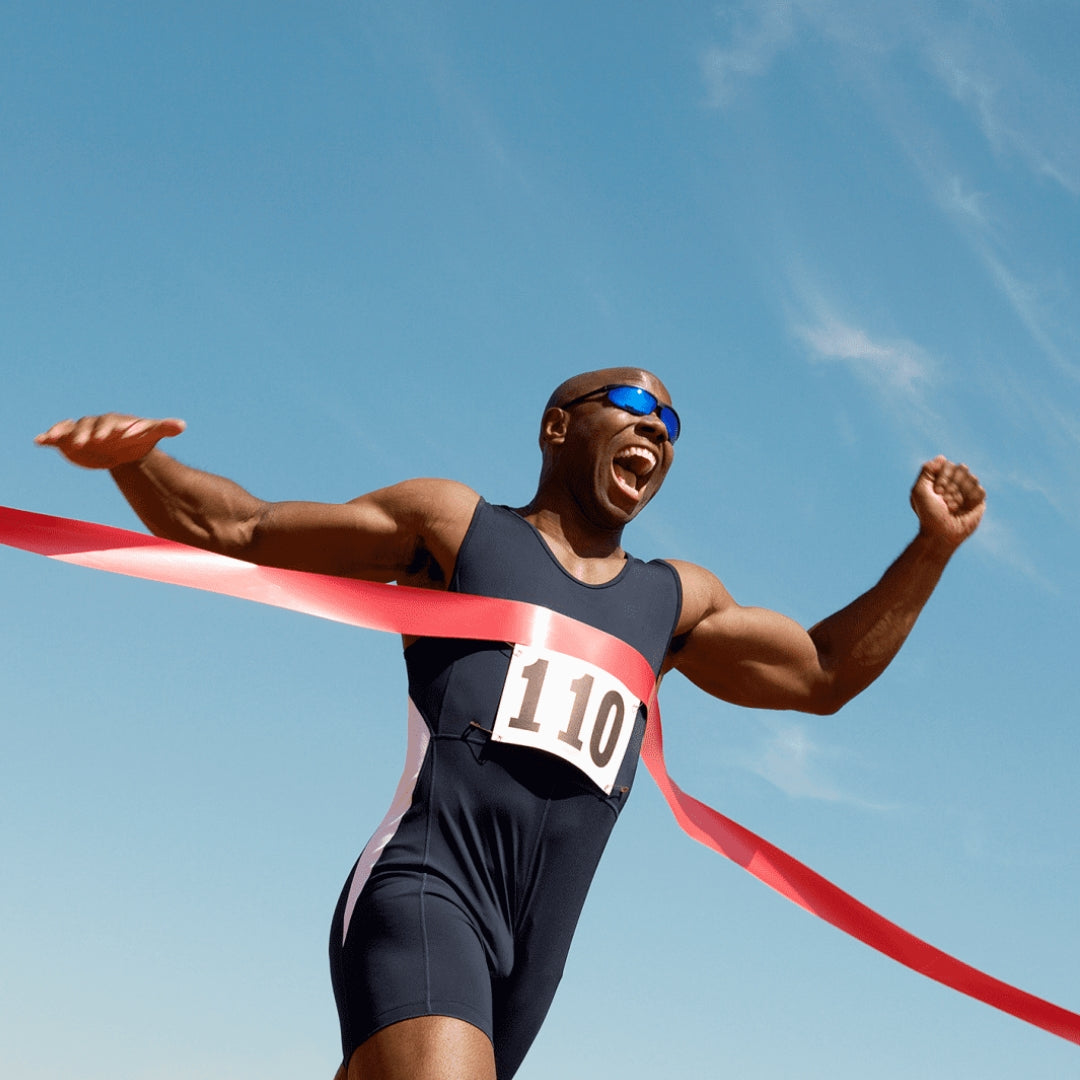 A runner wearing sunglasses passes the ribbon of a finish line