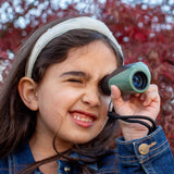 Young girl using a green monocular outdoors with blurred red foliage in the background