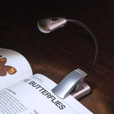 Clip-on book light illuminating a book about butterflies on a wooden surface