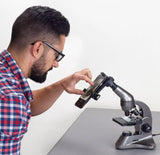 Man using a smartphone with a microscope attachment on a white background
